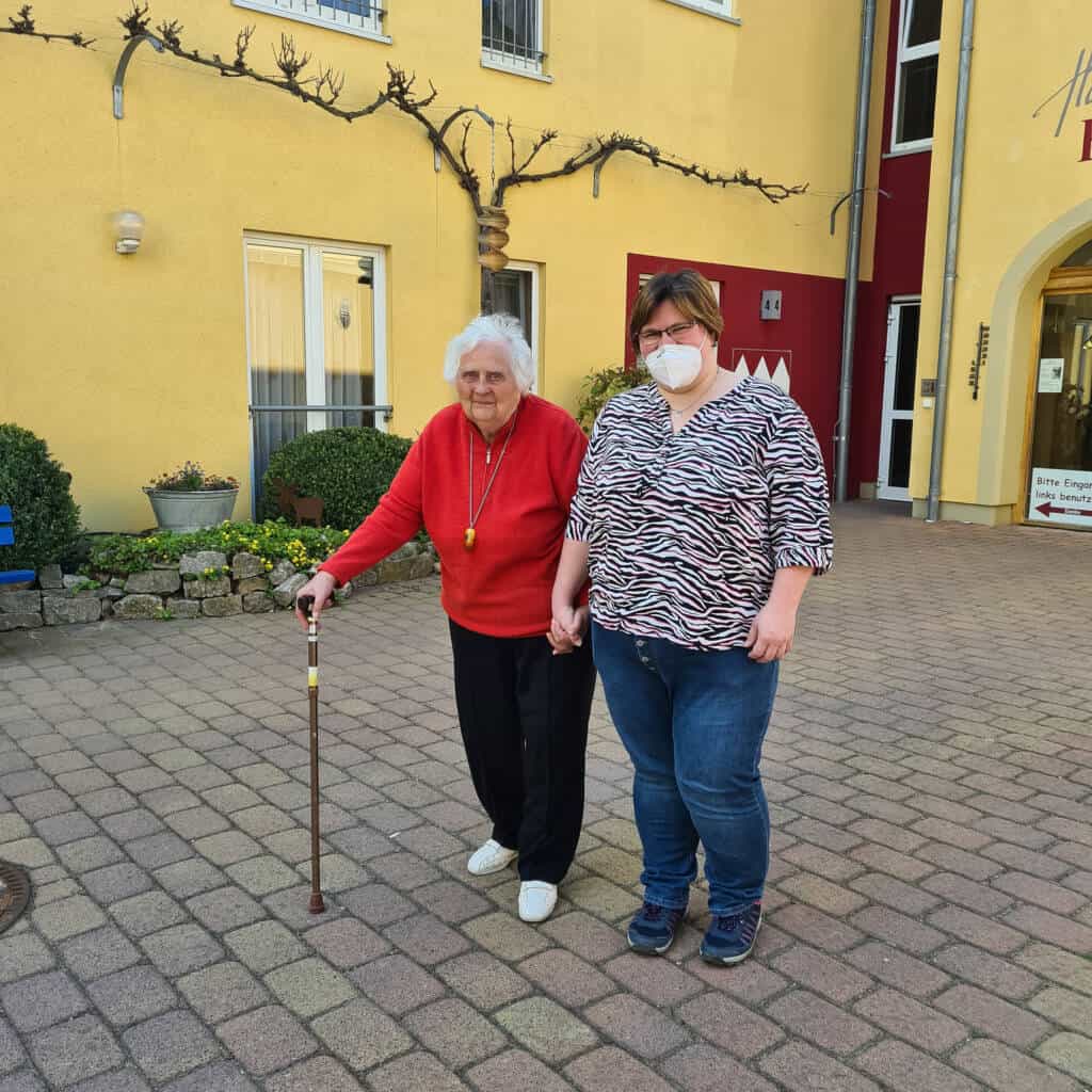 Pflegefachkraft Jacqueline und Seniorin vor dem Haus der Pflege